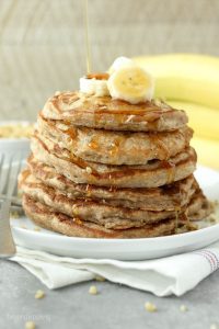 A stack of Banana Nut Protein Pancakes topped with syrup and bananas slices.