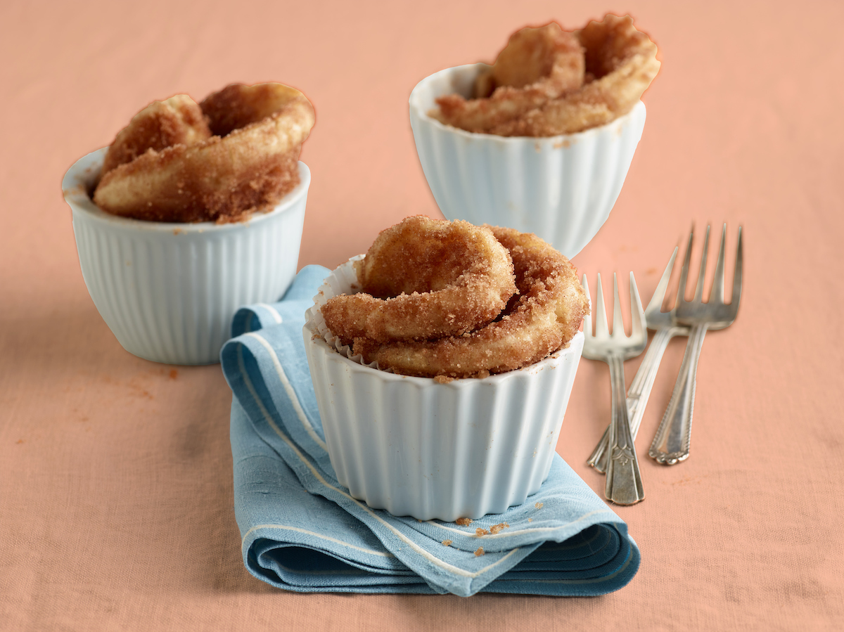Three Cinnamon Sugar Roll-Ups in individual muffin tins with forks and napkins.