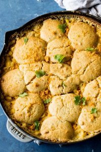 A Creamed Corn Cornbread Casserole, served in a cast iron skillet, sits on a blue table.