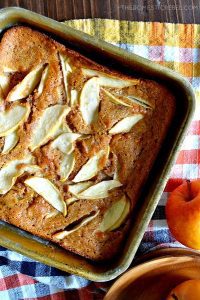 An oven-fresh Easy Apple Cobbler sits next to an apple on a colorful gingham tablecloth.