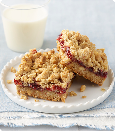 A plate of peanut butter and jelly bars, made with Krusteaz, sits next to a glass of milk.