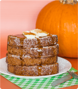 A stack of Pumpkin French Toast topped with powdered sugar and maple syrup.