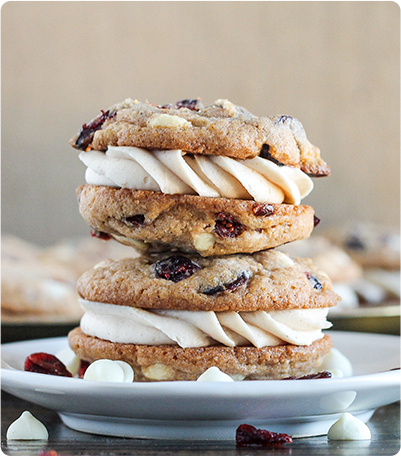 A stack of pumpkin spice cookie sandwiches with cream cheese filling sits on a plate.