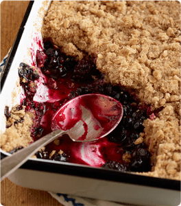 A serving spoon resting in an oven-fresh Berry Cobbler that is missing a couple servings.