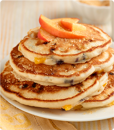 A stack of Blueberry Peach Pancakes topped with peach slices.