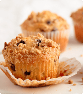 A couple Blueberry Praline Muffins with one muffin sitting on its opened wrapper.