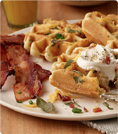 A plate of Cheddar and Sage Waffles topped with sour cream, chives and sage with a side of bacon.