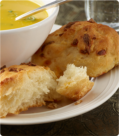 A plate with two loaves of Cheese Petit Pains with one ripped in half and paired with a bowl of soup.