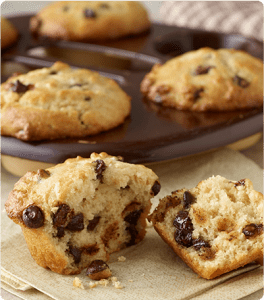 A muffin pan of Chocolate Chip Banana Muffins with a half broken muffin in front.