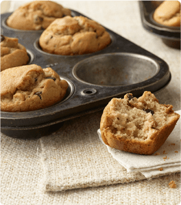 A muffin pan of Chocolate Peanut Butter Chip Muffins with one half of a muffin laid in front of the pan.