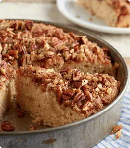 A Cinnamon Apple Pecan Crumb Cake in a round tin pan with a slice cut out.