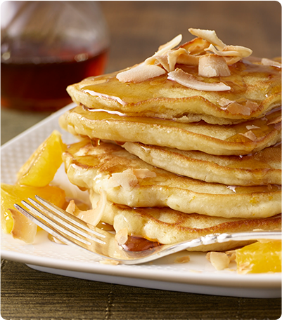 A stack of Coconut Orange Pancakes topped with coconut flakes and syrup.