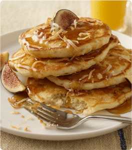 A stack of Coconut Pecan Pancakes topped with syrup and coconut flakes.