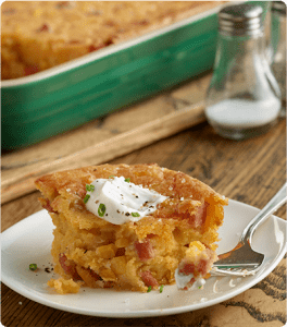 A slice of Double Corn and Ham Bake sits on a white plate next to a silver fork.