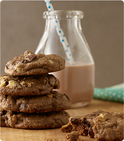 A stack of Double Trouble Chocolate Cookies next to a glass of chocolate milk.