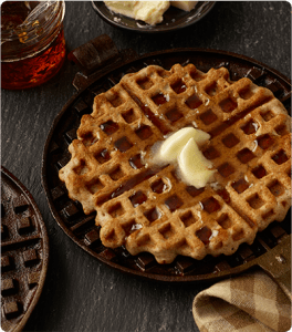 An Easy Apple Waffle on a cast iron waffle iron, topped with butter and syrup.