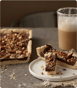 A slice of Elegant Chocolate Pastry on a white plate served with a coffee.