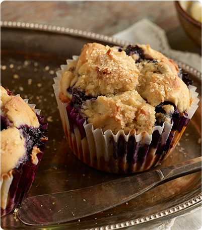 A Gluten Free Blueberry Muffin on a silver serving dish next to a butter knife.