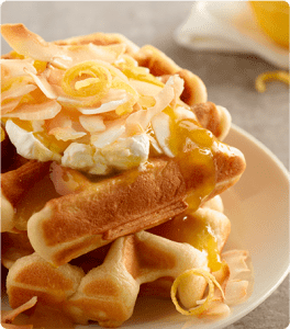 Two Lemon Creme Waffles stacked on top of each other and topped with cream cheese, lemon pie filling and flaked coconut.