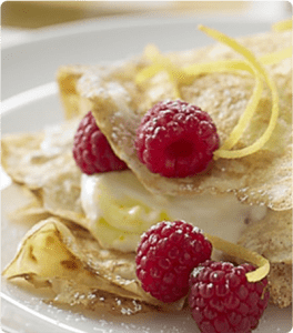 A plate of Lemon Crepes topped with raspberries, lemon zest and yogurt.