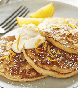 Three Lemon Ricotta Pancakes topped with cream and lemon zest.