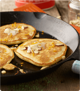 A cast iron skillet with three Orange Almond Pancakes topped with glaze and sliced almonds.