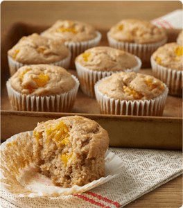 A wooden tray of several Orange Spice Muffins with one of the muffins off of the tray and half eaten.