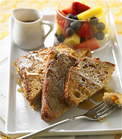 A plate of Oven Baked Banana French Toast served with a bowl of fruit and a cup of coffee.
