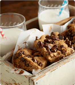 A wooden crate filled will freshly baked Peanut Butter Chocolate Bars and two glasses of milk.