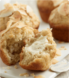 A plate of Piña Colada Muffins with one of the muffins torn in half and butter spread on the inside.