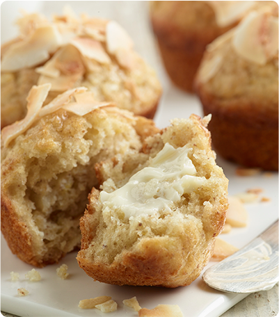 A plate of Piña Colada Muffins with one of the muffins torn in half and butter spread on the inside.