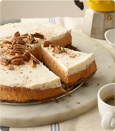 A Pumpkin Cheesecake topped with pecans and a couple slices already cut out.