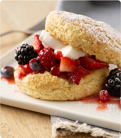 A Shortcake with a layer of whipped cream, raspberries, strawberries, blueberries, blackberries and cranberries in between.