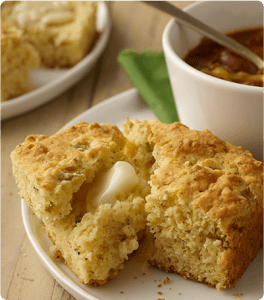 A plate of Southwestern Cornbread topped with melted butter and served with a bowl of chili.