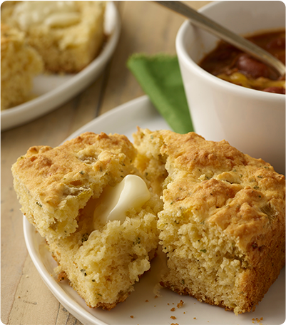 A plate of Southwestern Cornbread topped with melted butter and served with a bowl of chili.