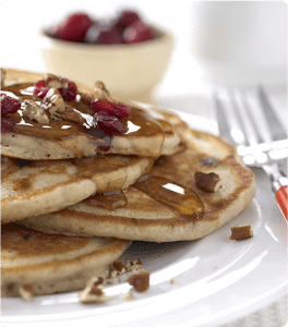 A stack of Toasted Pecan Cranberry Pancakes topped with dried cranberries, chopped pecans and syrup.