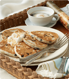 A plate of Tropical Dream Pancakes topped with whipped cream and coconut flakes.