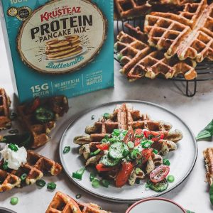 A plate of Spinach Feta Waffles topped with scallions, cucumbers, dried mint, crumbled feta and tomatoes.