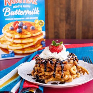 A stack of Funnel Cakes topped with chocolate sauce, whipped cream and strawberries.