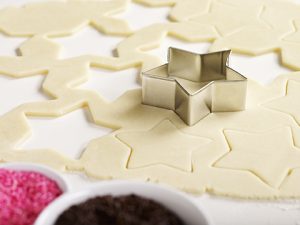 A sheet of cookie dough being cut with a star-shaped cookie cutter.