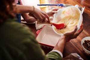 Hands transferring Cinnamon Swirl Crumb Cake batter into a baking dish