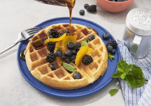 A Belgian Waffle topped with fresh blueberries, oranges, blackberries, and syrup on a blue plate.