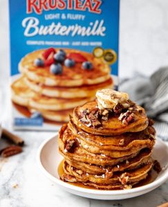 A stack of Sweet Potato Pancakes topped with butter, chopped pecans and maple syrup.