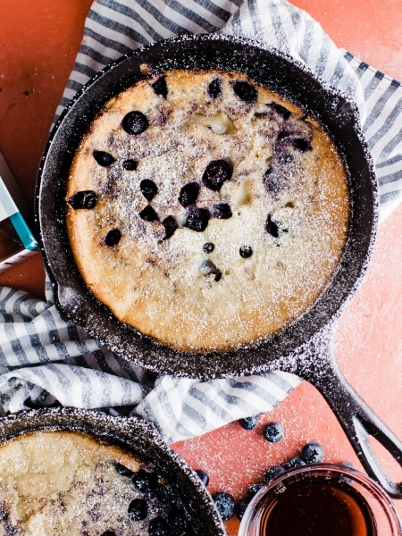 A cast iron skillet filled with a Blueberry Skillet Pancake topped with powdered sugar.