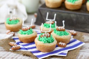 Several Football Cookie Cups on a blue and white stripped napkin.