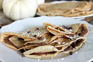 A plate of Pumpkin Chocolate Chip Crepes topped with mini chocolate chips and powdered sugar.