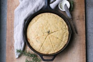A loaf of Gluten Free Rosemary Asiago Cornbread in a cast iron skillet.