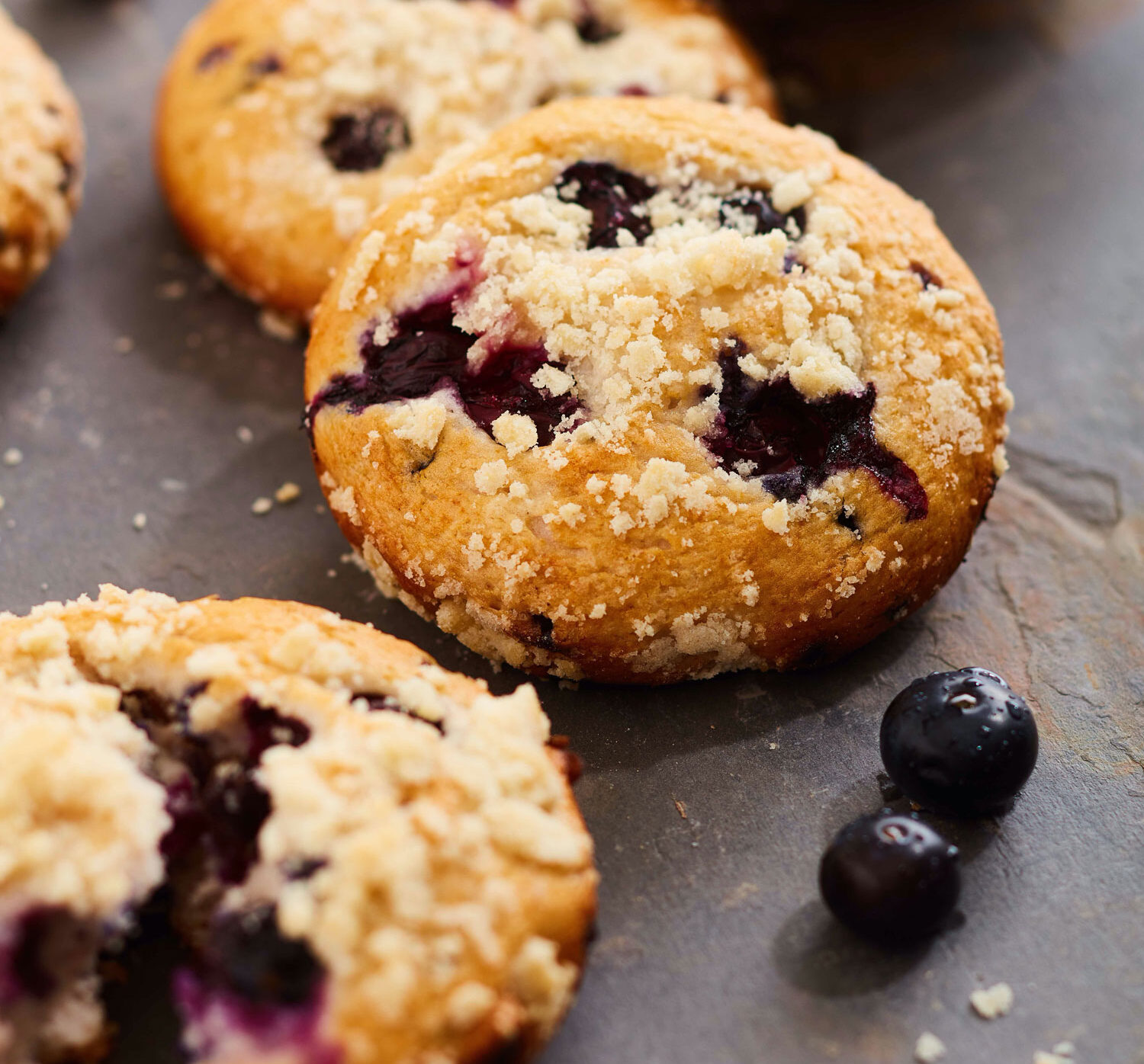 Fresh-baked Blueberry Cheesecake Muffins sitting on a stone counter.