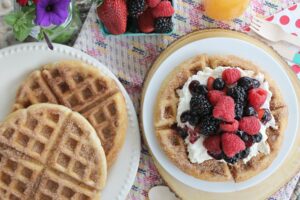 Two plates of Churro Waffles with one stack of waffles topped with whipped cream and berries.