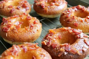 Several Honey Glazed Cornbread Donuts with Crumbled Bacon resting on a cooling rack.